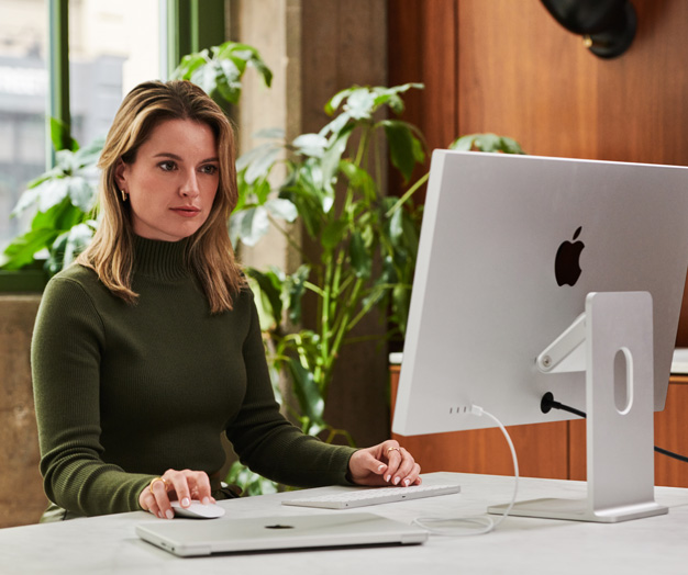 A person sitting at a desk in front of an iMac.