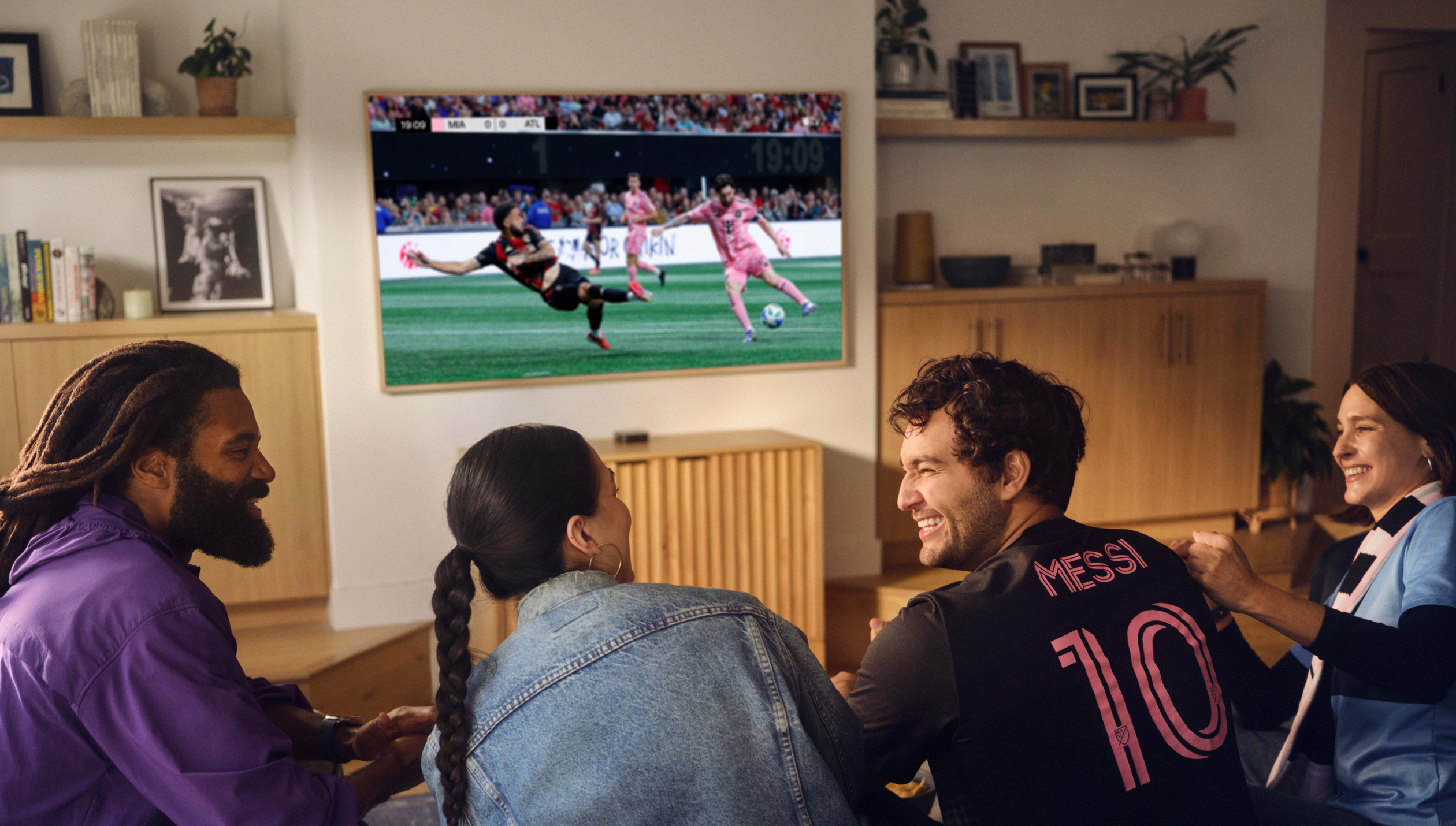 Un groupe de quatre amis souriants, assis sur un canapé et regardant le MLS Season Pass sur un téléviseur.